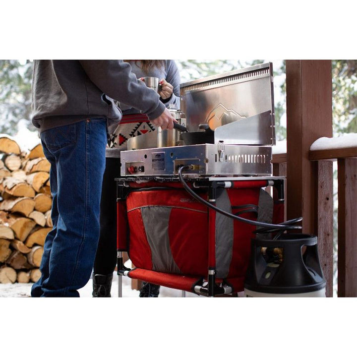 Chattanooga Camp Chef Mountaineer aluminum two-burner portable outdoor cooking system with side shelves and sturdy handles.